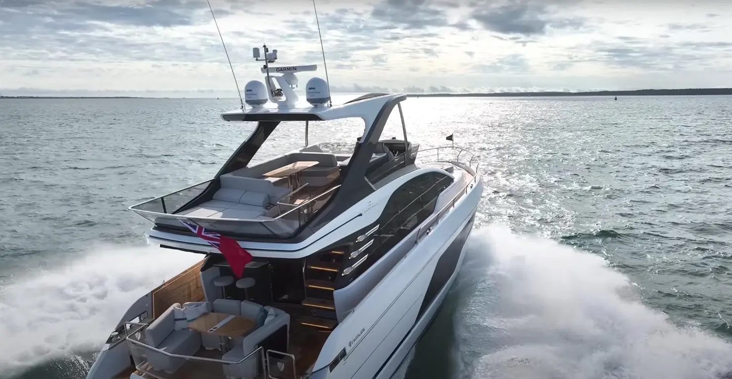 A luxury yacht navigating through calm waters, displaying a British flag and modern design, under a cloudy sky.